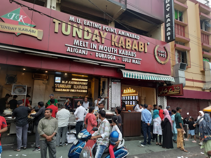 A group of people standing in front of a restaurant called Tunday Kababi.